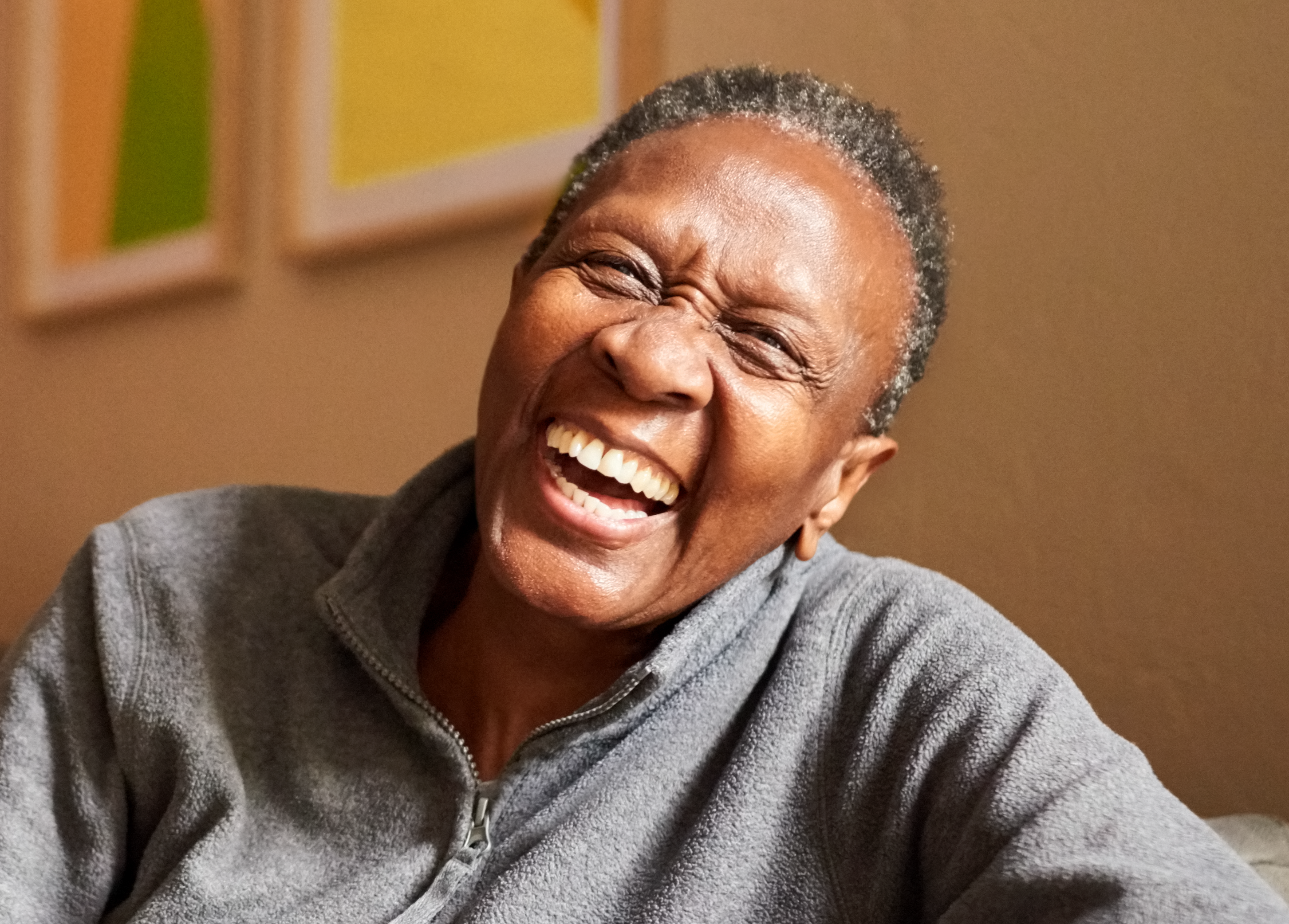 An older male sitting on a brown couch and smiling.